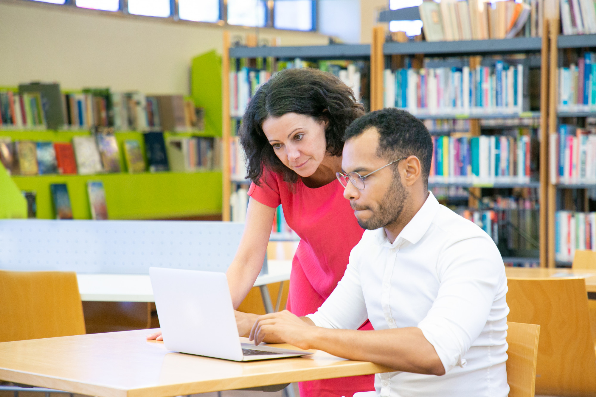 A university tutor guiding a student working on a laptop inside a bright library, representing personalized learning and academic support for 
                        students enrolled in management courses UK universities offer